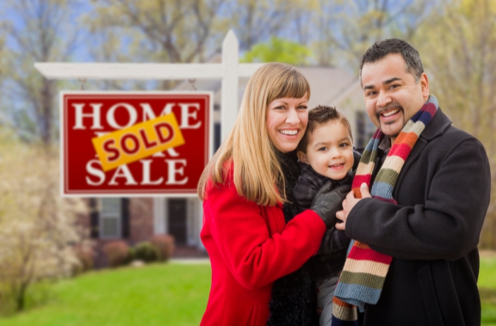 happy family smiling in front of house sold sign - first time home buyer in calgary